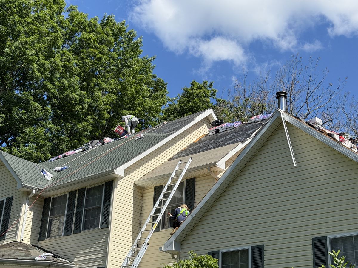 Roofer in safety harness working the ridge with materials staged at the chimney